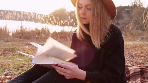 Slow Motion Caucasian Blonde Woman with Beige Hat in Black Sweater Reads Book in the Countryside