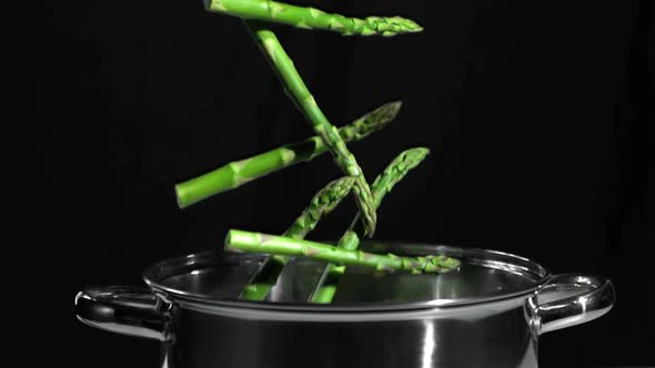 Asparagus falling in pot on black background