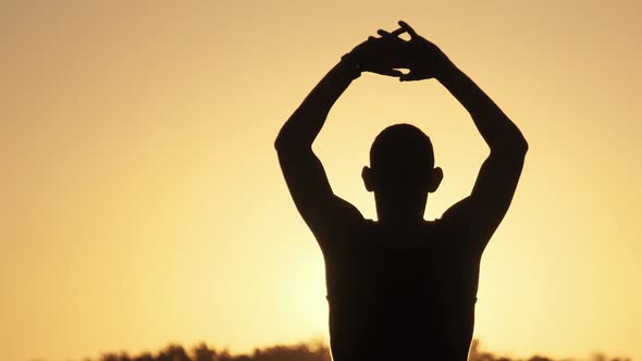 Silhouette of Young Man Against Sunset Raising Hands Sides and Up. Slow Motion