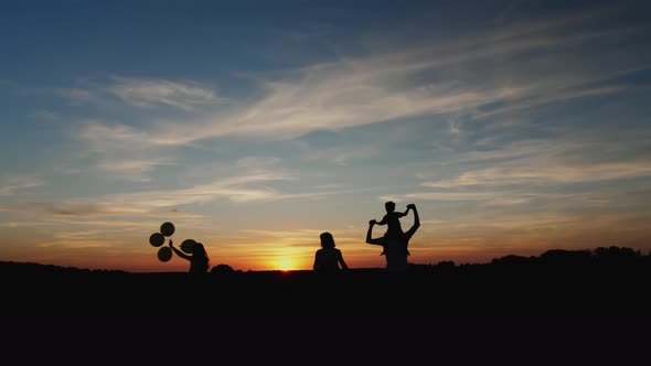 Silhouettes of Family Running in the Meadow During Sunset