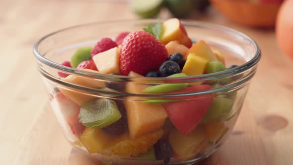 Camera follows putting fresh mint over fruit salad. Slow Motion.