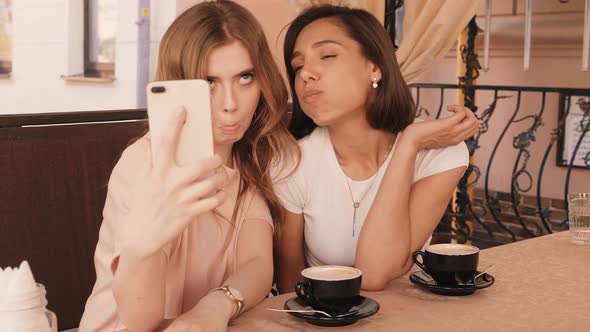 Two young beautiful smiling hipster girls chatting in cafe