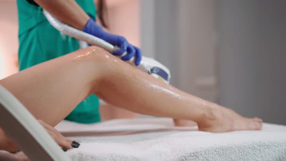 Beautician Doing Laser Hair Removal on Slim Legs Woman in Beauty Salon. 