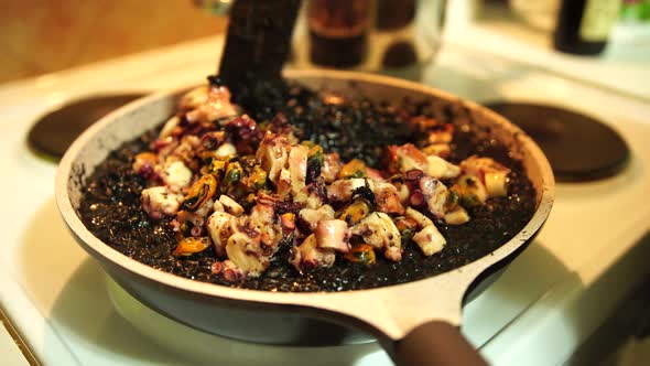 Stirring Black Risotto with Sea Food in Pan on Stove with Spatula