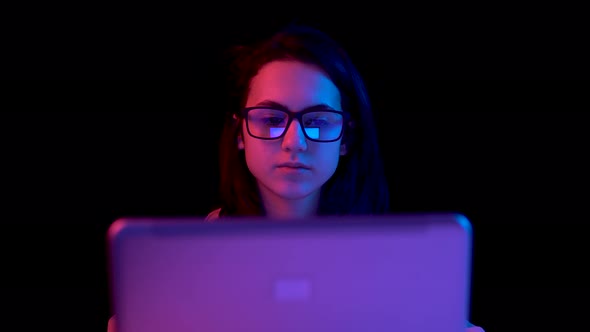 Young Woman with a Laptop. A Woman Is Using a Laptop. Blue and Red Light Falls on a Woman on a Black