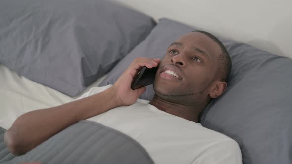 African Man Talking on Smartphone While Sleeping in Bed Close Up