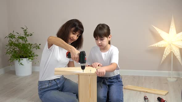 Happy Family Mother and Daughter Assembling Wooden Furniture Together with Screwdriver