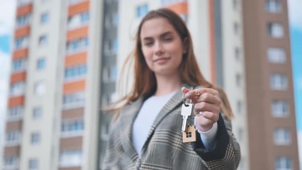 The Girl Shows the Keys to the Apartment Against the Backdrop of an Apartment Building