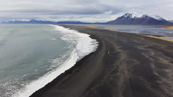 Drone Over Black Sand Beach With Mountain Range In Background