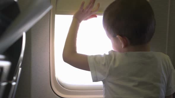 Young Cute Boy Sitting on the Seat and Opens Up Airplane Window