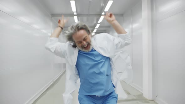 Excited Mature Male Doctor in Uniform Dancing Walking Along Hospital Corridor