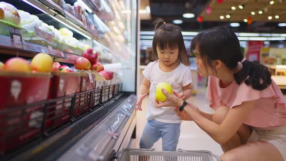 Asian young beautiful mother holding grocery basket with her little kid child walking in supermarket