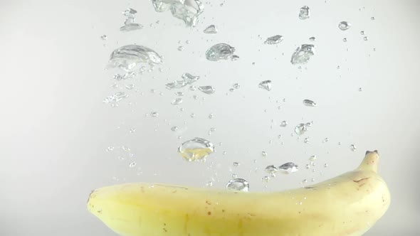 One banana falls into the water with splashes and bubbles in slow motion