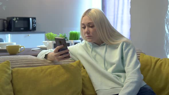 Young female user using mobile phone while sitting on sofa at home.