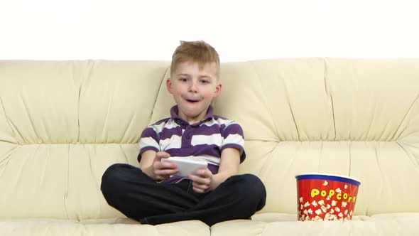 Child Plays on Phone in Online Game and Eats Popcorn