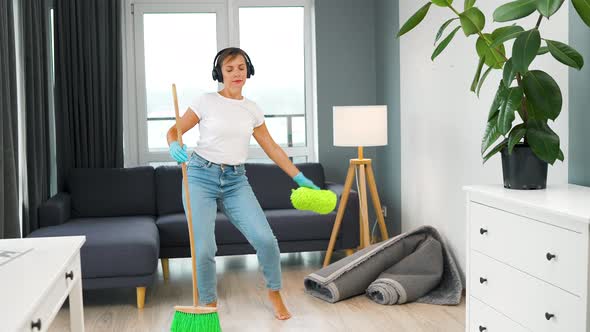 Woman in Headphones Cleaning the House and Having Fun Dancing with a Broom and Washcloth