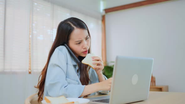 Asian attractive businesswoman hungry eating bread in hurry time while running business on laptop.