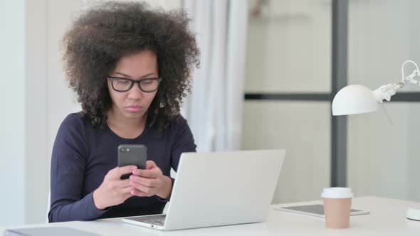 African Woman with Laptop Using Smartphone at Work