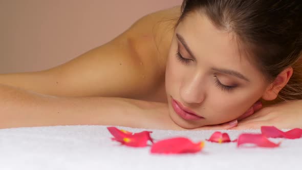 Woman Relaxing After Massage Lying on Towels with Rose Petals