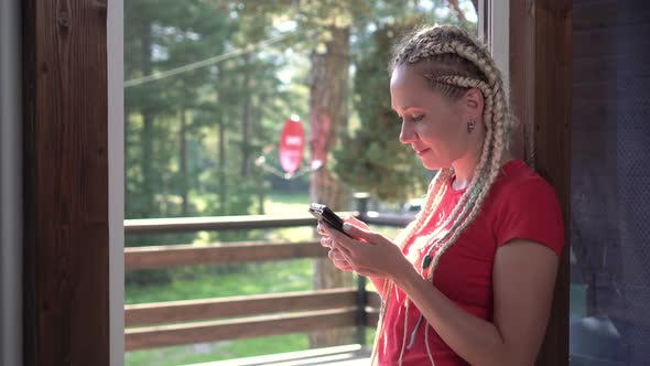 Woman with a Smartphone in a Country House on the Background of Forest and Nature