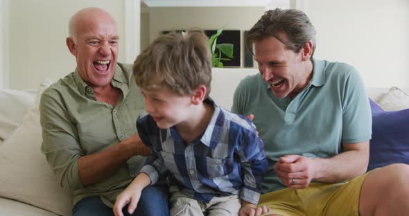 Portrait of happy caucasian grandfather with adult son and grandson playing in living room