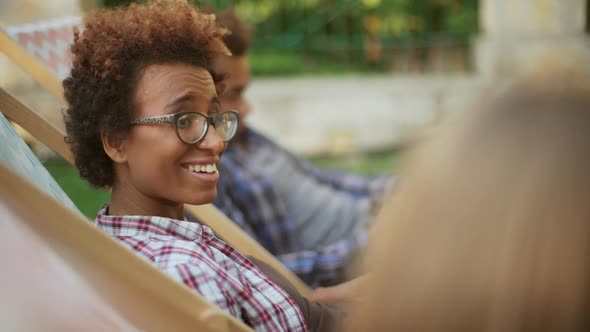 Young African American Female Sitting in Park on Lounge Chatting Smiling with Friends While