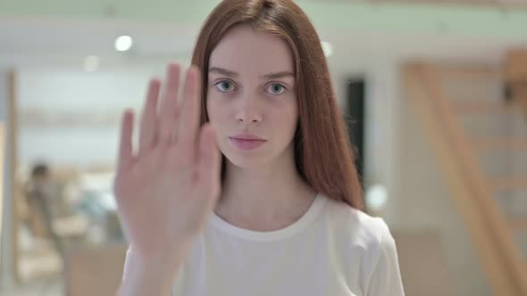 Portrait of Focused Redhead Young Woman Doing Stop Sign with Hand