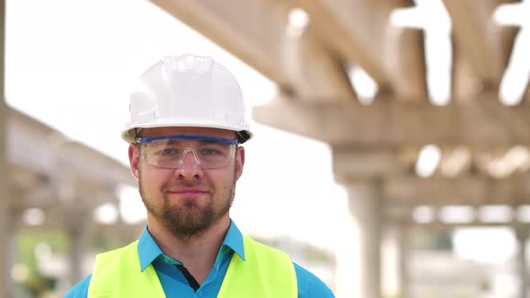 Close Up Portrait of Smiling Young Master Builder in Protective White Hard Hat Looking at Camera