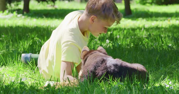 Cheerful Boy Lying on Grass and Playing with Cute Puppy