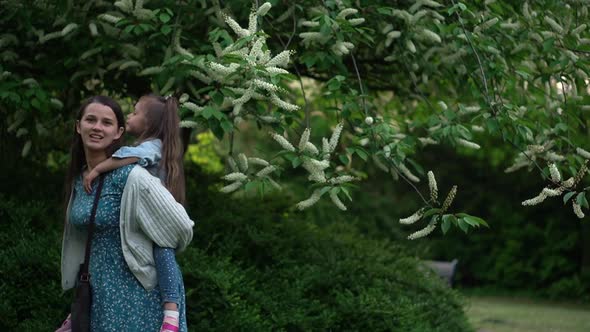 Happy Family Mother with Two Daughters Little Siblings Kids Have Fun Sniffing Flowers on Trees