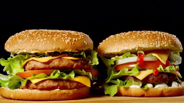 Close-up of Two Appetizing Burgers with Sesame Buns Rotating on Black Background