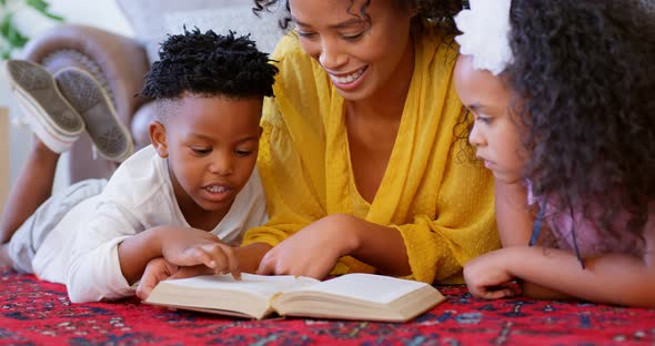 Front view of black mother with her children reading a book in a comfortable home 4k