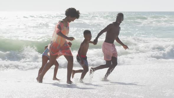 Smiling african american family holding hands and running on sunny beach