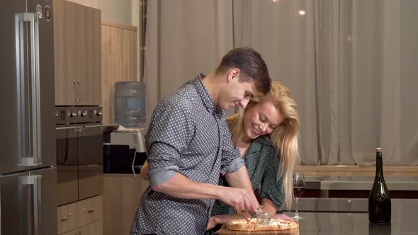 Handsome Man Cutting Pizza at Home, His Loving Wife Hugging Him