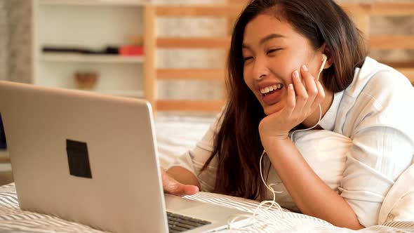 Happy Asian Woman Working on a Laptop on Her Bed