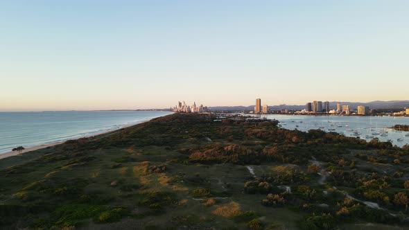 Panoramic drone view travelling over a coastal nature parklands with a urban city skyline rising abo