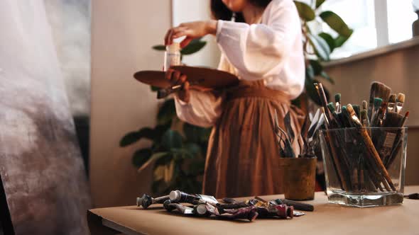 Art Studio Young Woman Artist Mixing Paints and Solvent on the Palette and Applying the Mixture on