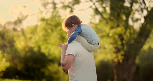 A Child Sitting on the Neck of His Father While Walking in Summer Field at Sunset