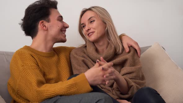 Happy Affectionate Young Couple Kissing Talking Cuddling at Home on Sofa