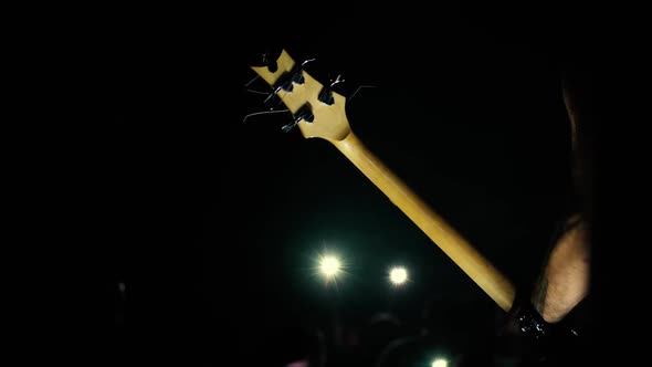 The bass guitar fingerboard and the guitarist's hand against the background of a dark hall