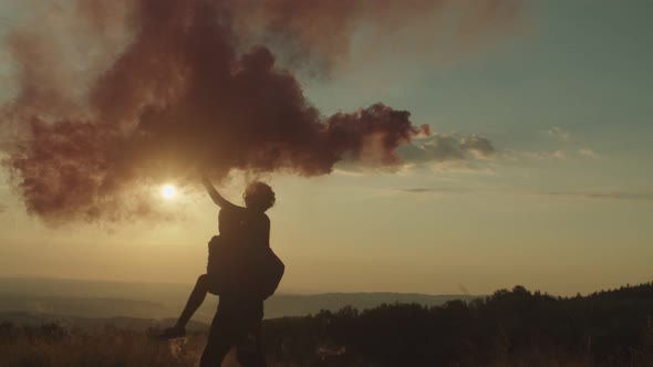 Silhouette of Carefree Multi Ethnic Couple with Smoke Bomb Enjoying Leisure and Freedom at Sundown