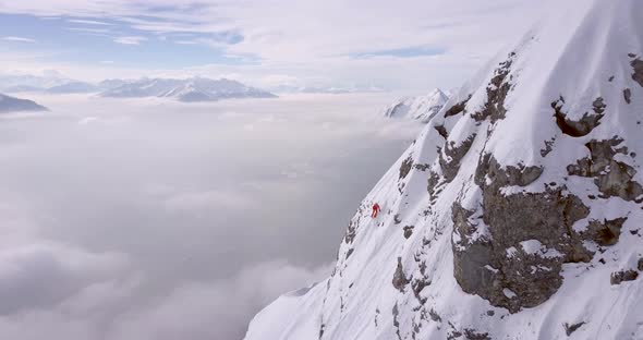 Aerial drone view of a skier skiing down a steep snow covered mountain