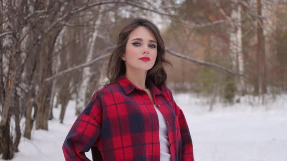 Young Woman with Wavy Hair Standing and Touching Face in Winter Forest