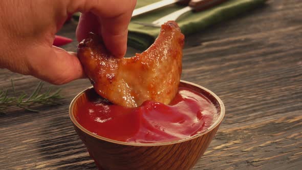 Close-up of a Male Hand Dipping a Chicken Wing Into the Ketchup