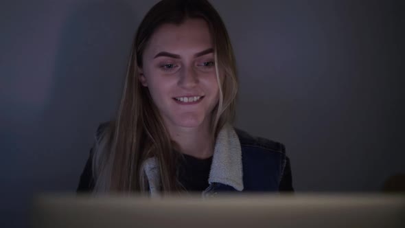 Happy Smiling Girl Watching on Laptop Screen at Night