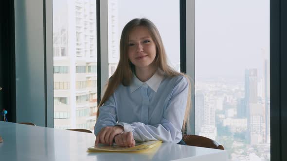 Smiling Young Businesswoman Sitting Alone in Office and Looking at Camera