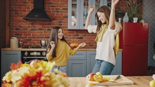 Young Mother and Little Daughter are Laughing Dancing and Whirling While Cooking in Modern Kitchen