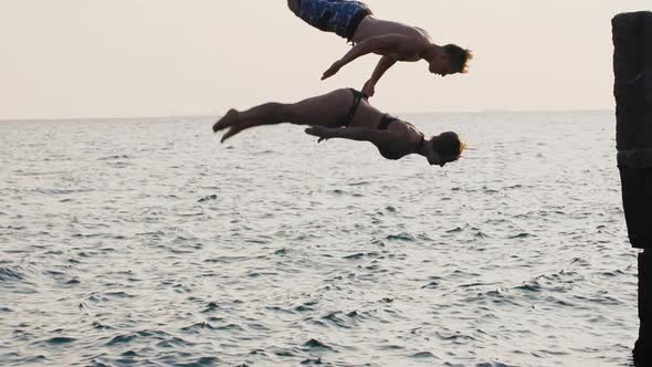 Young Woman and Man Synchronously Doing Backflip From a Pier Into the Sea During Beautiful Sunrise