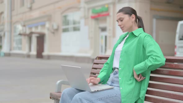 Hispanic Woman with Back Pain Using Laptop While Sitting Outdoor on Bench