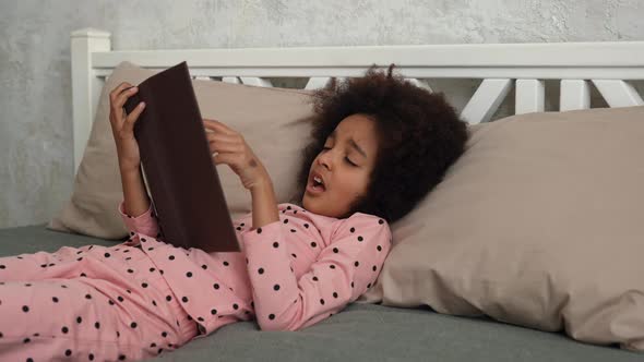 Cute Little African American Girl Reads a Book with Fairy Tales and Falls Asleep